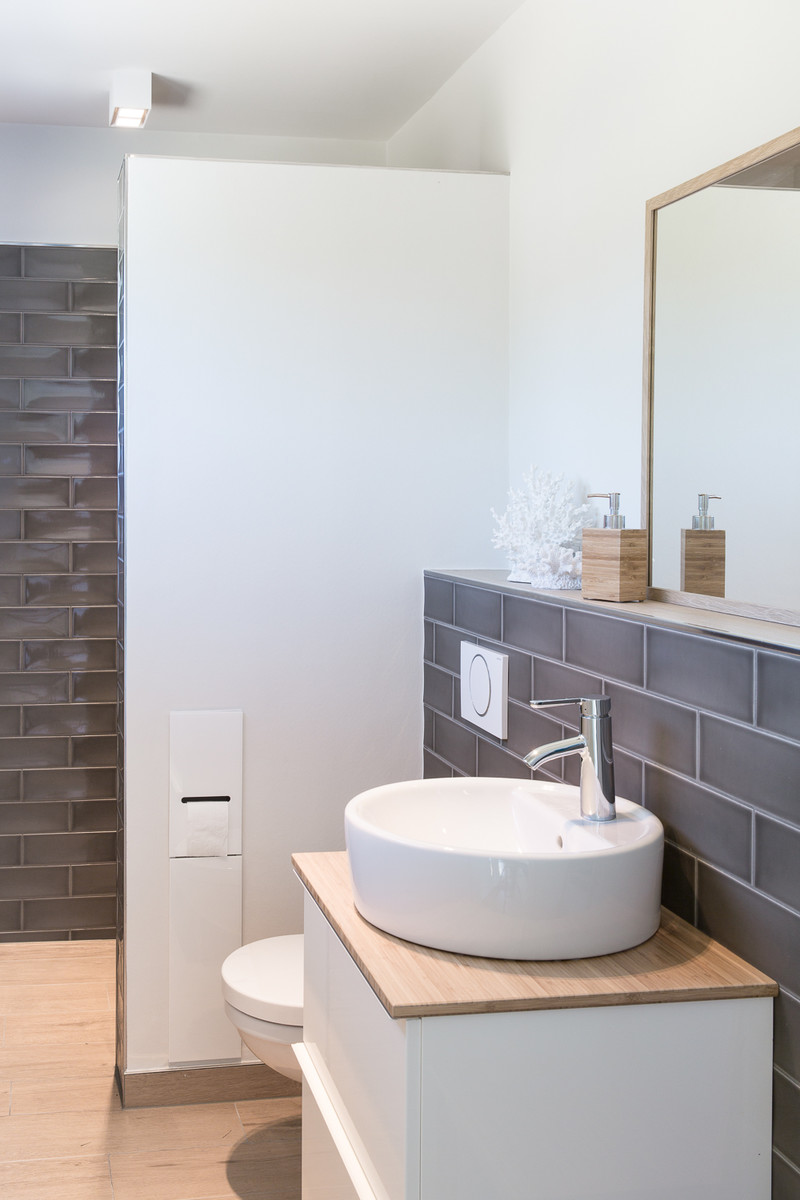 Inspiration for a small scandinavian cloakroom in Hamburg with flat-panel cabinets, white cabinets, a wall mounted toilet, grey tiles, metro tiles, white walls, a vessel sink and brown floors.