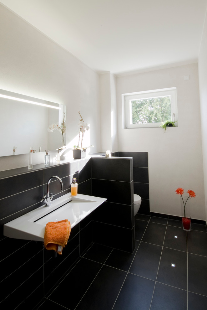 На фото: туалет среднего размера в современном стиле с черной плиткой, белыми стенами и раковиной с несколькими смесителями с