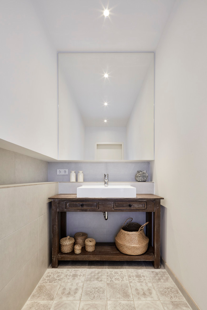 Photo of a small rustic cloakroom in Cologne with recessed-panel cabinets, dark wood cabinets, beige tiles, cement tiles, white walls, ceramic flooring, a vessel sink, wooden worktops, beige floors and brown worktops.