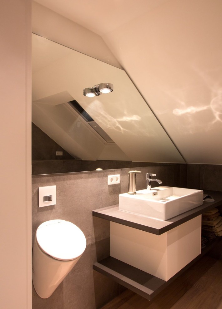 Lantlig inredning av ett mellanstort grå grått toalett, med en bidé, grå kakel, skifferkakel, vita väggar, ljust trägolv, ett fristående handfat, bänkskiva i akrylsten och brunt golv