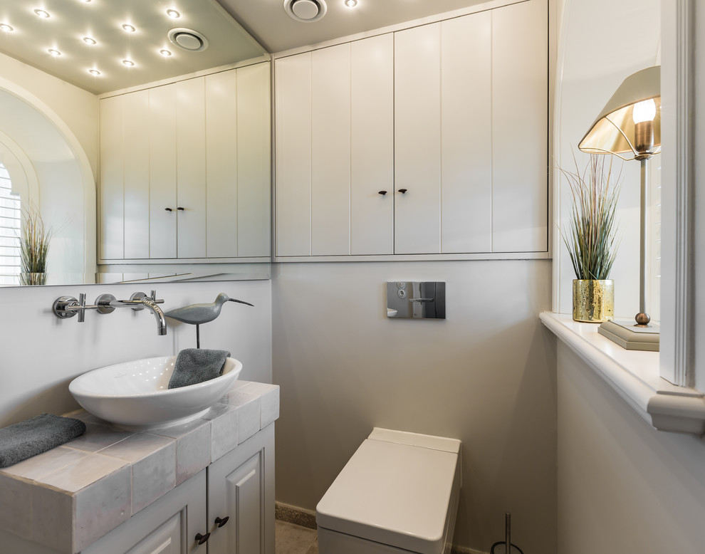 Inspiration pour un WC suspendu rustique de taille moyenne avec des portes de placard beiges, un mur beige, une vasque, un carrelage gris et un placard avec porte à panneau surélevé.