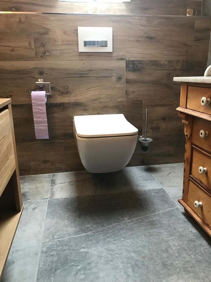 This is an example of a small country cloakroom in Dortmund with brown cabinets, a two-piece toilet, grey tiles, ceramic tiles, brown walls, ceramic flooring, a vessel sink, wooden worktops, grey floors and brown worktops.