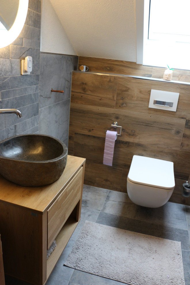 Cette photo montre un petit WC et toilettes nature avec des portes de placard marrons, WC séparés, un carrelage gris, des carreaux de céramique, un mur marron, un sol en carrelage de céramique, une vasque, un plan de toilette en bois, un sol gris et un plan de toilette marron.