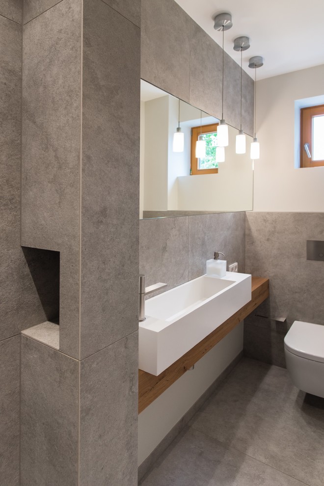 Idee per un piccolo bagno di servizio minimal con WC sospeso, piastrelle grigie, piastrelle di cemento, pareti bianche, pavimento in cementine, lavabo a bacinella, top in legno e pavimento grigio