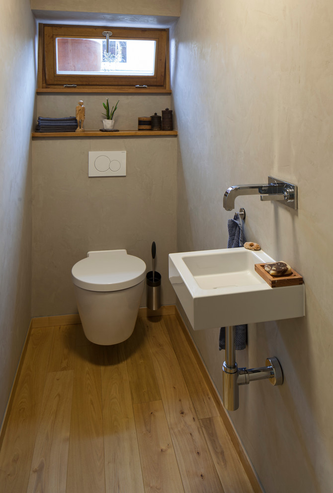 Imagen de aseo actual con sanitario de pared, paredes grises, suelo de madera en tonos medios y lavabo suspendido