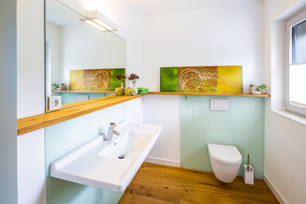 Idee per un piccolo bagno di servizio contemporaneo con WC a due pezzi, piastrelle verdi, lastra di vetro, pareti bianche, pavimento in legno massello medio, lavabo sospeso e pavimento marrone