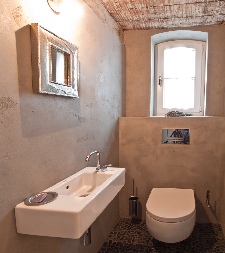 Exempel på ett litet rustikt toalett, med en vägghängd toalettstol, grå väggar, klinkergolv i småsten och ett väggmonterat handfat