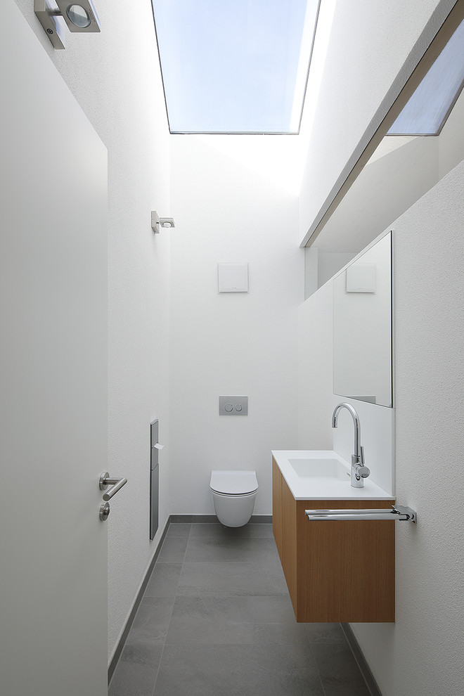 Пример оригинального дизайна: туалет среднего размера в стиле модернизм с плоскими фасадами, фасадами цвета дерева среднего тона, раздельным унитазом, белыми стенами, монолитной раковиной и серым полом