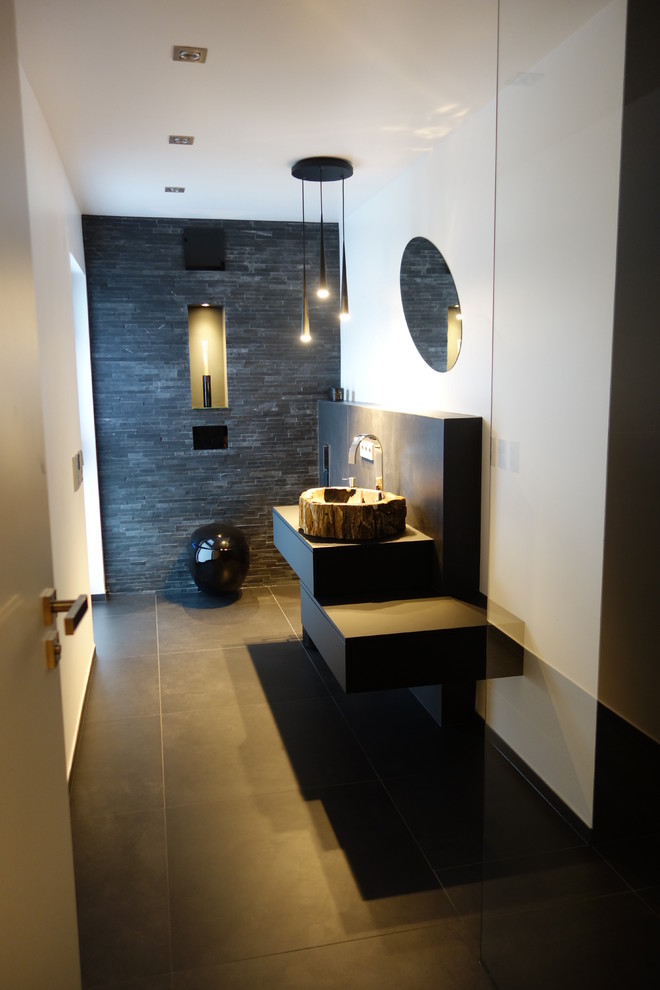 Idéer för ett mellanstort modernt toalett, med släta luckor, svarta skåp, en vägghängd toalettstol, svart kakel, skifferkakel, vita väggar, cementgolv, ett väggmonterat handfat, träbänkskiva och svart golv