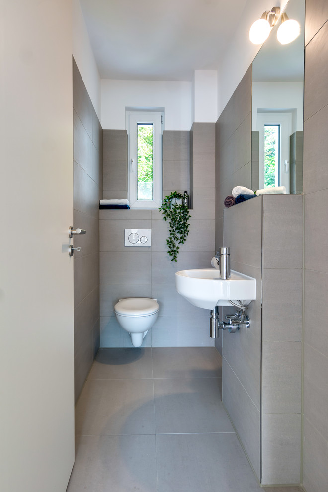 ハンブルクにある小さな北欧スタイルのおしゃれなトイレ・洗面所 (壁掛け式トイレ、ベージュのタイル、セメントタイル、白い壁、セメントタイルの床、壁付け型シンク、ベージュの床) の写真