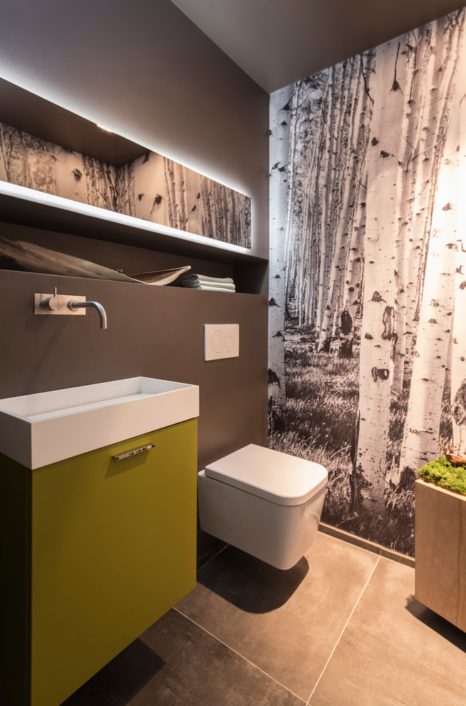 デュッセルドルフにある小さなコンテンポラリースタイルのおしゃれなトイレ・洗面所 (フラットパネル扉のキャビネット、黄色いキャビネット、壁掛け式トイレ、茶色い壁、セメントタイルの床、ベッセル式洗面器、黒い床) の写真
