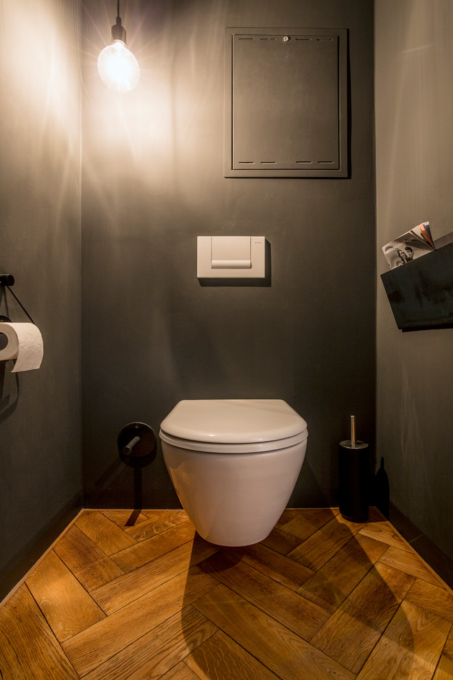 ミュンヘンにある高級な中くらいなコンテンポラリースタイルのおしゃれなトイレ・洗面所 (オープンシェルフ、壁掛け式トイレ、黒いタイル、白い壁、無垢フローリング、壁付け型シンク、コンクリートの洗面台、茶色い床) の写真