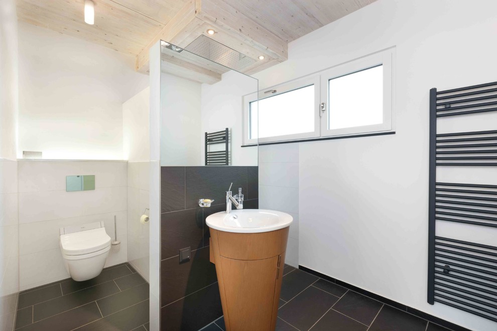 Photo of a large contemporary cloakroom in Stuttgart with flat-panel cabinets, brown cabinets, a two-piece toilet, black and white tiles, ceramic tiles, white walls, ceramic flooring, a pedestal sink and black floors.