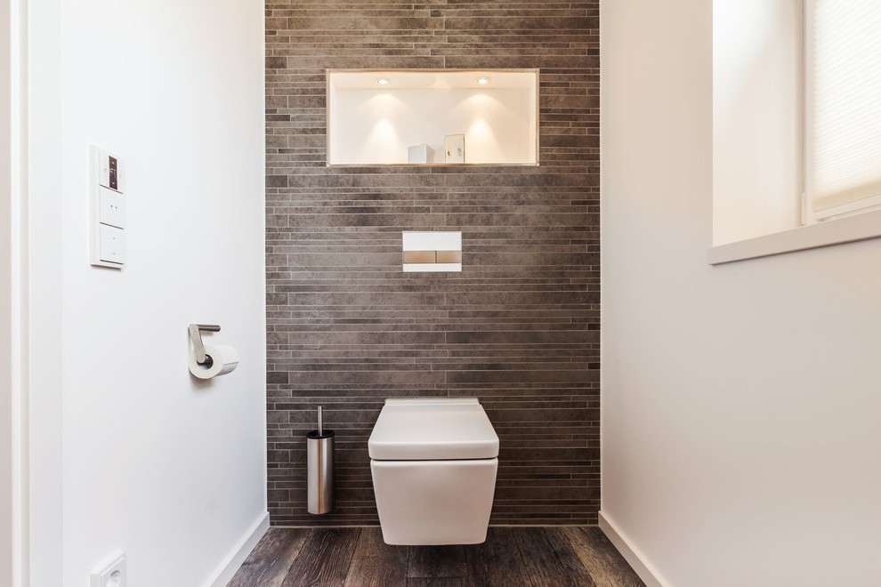Idéer för ett mellanstort modernt toalett, med skåp i mellenmörkt trä, en vägghängd toalettstol, grå kakel, keramikplattor, målat trägolv och vita väggar