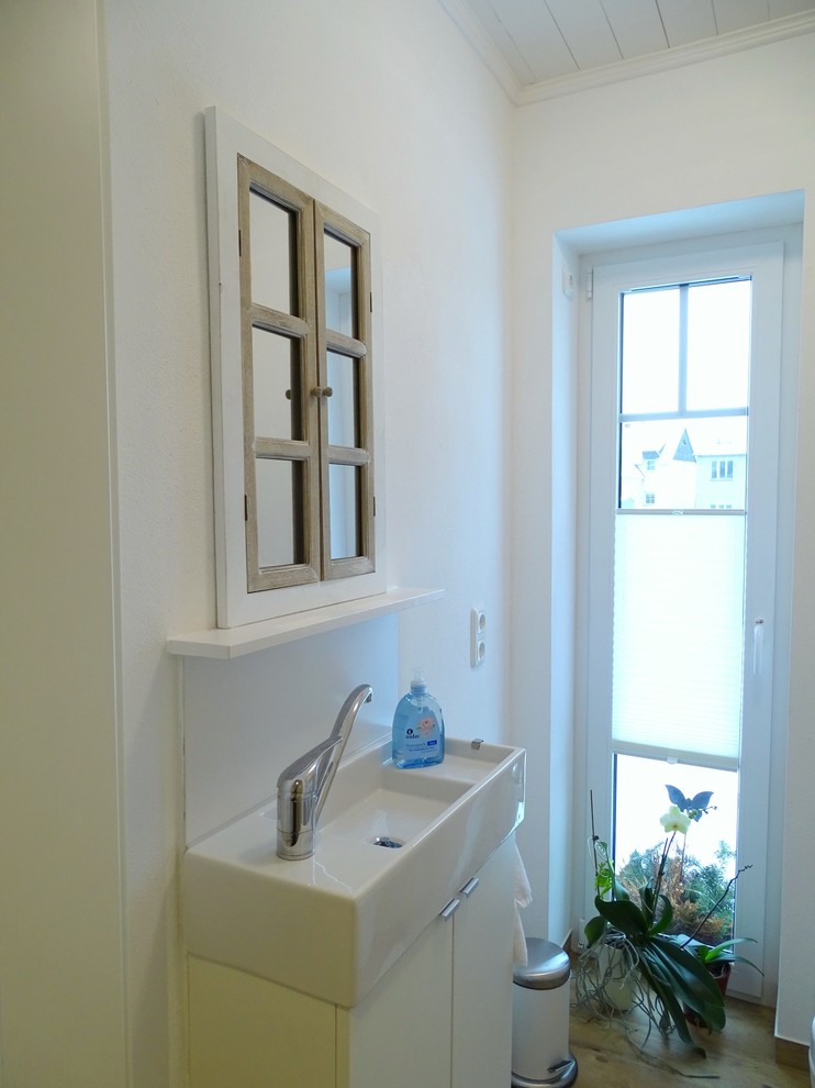 Inredning av ett nordiskt litet toalett, med släta luckor, vita skåp, en toalettstol med hel cisternkåpa, vit kakel, vita väggar och ett fristående handfat