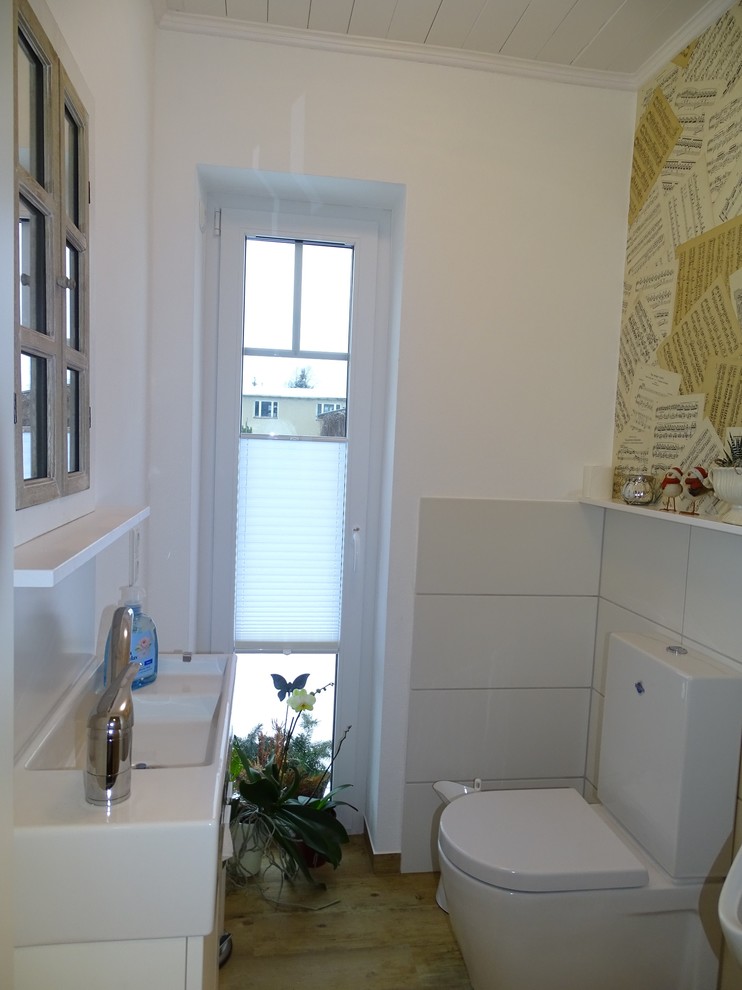 Exemple d'un petit WC et toilettes scandinave avec un placard à porte plane, des portes de placard blanches, WC à poser, un carrelage blanc, un mur blanc, un sol en vinyl et une vasque.