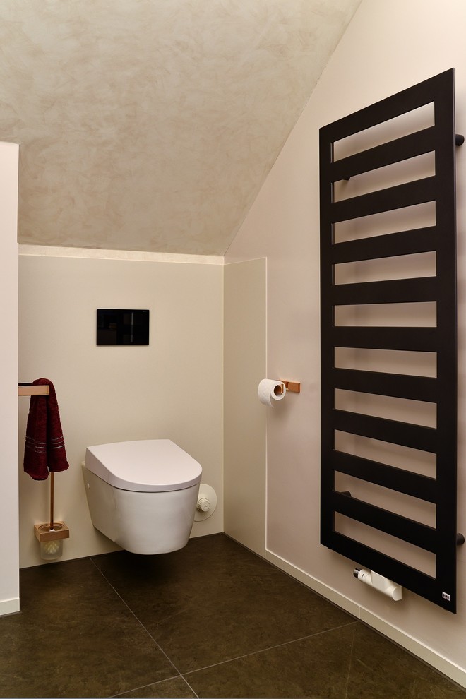 Imagen de aseo actual de tamaño medio con sanitario de pared, paredes beige, suelo de baldosas de cerámica y suelo marrón