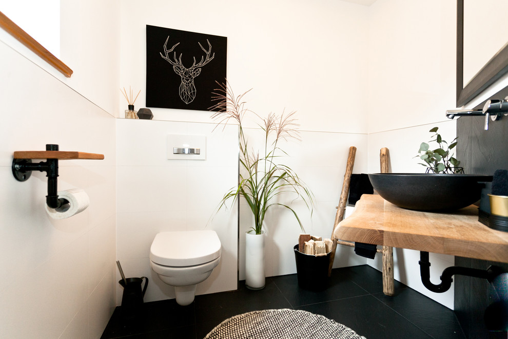 Idee per un piccolo bagno di servizio scandinavo con WC sospeso, piastrelle bianche, piastrelle in gres porcellanato, pareti bianche, pavimento in cementine, lavabo a bacinella, top in legno e pavimento nero