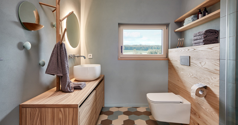 Exempel på ett litet lantligt brun brunt toalett, med släta luckor, skåp i mellenmörkt trä, en toalettstol med separat cisternkåpa, grå väggar, ett fristående handfat, träbänkskiva och flerfärgat golv