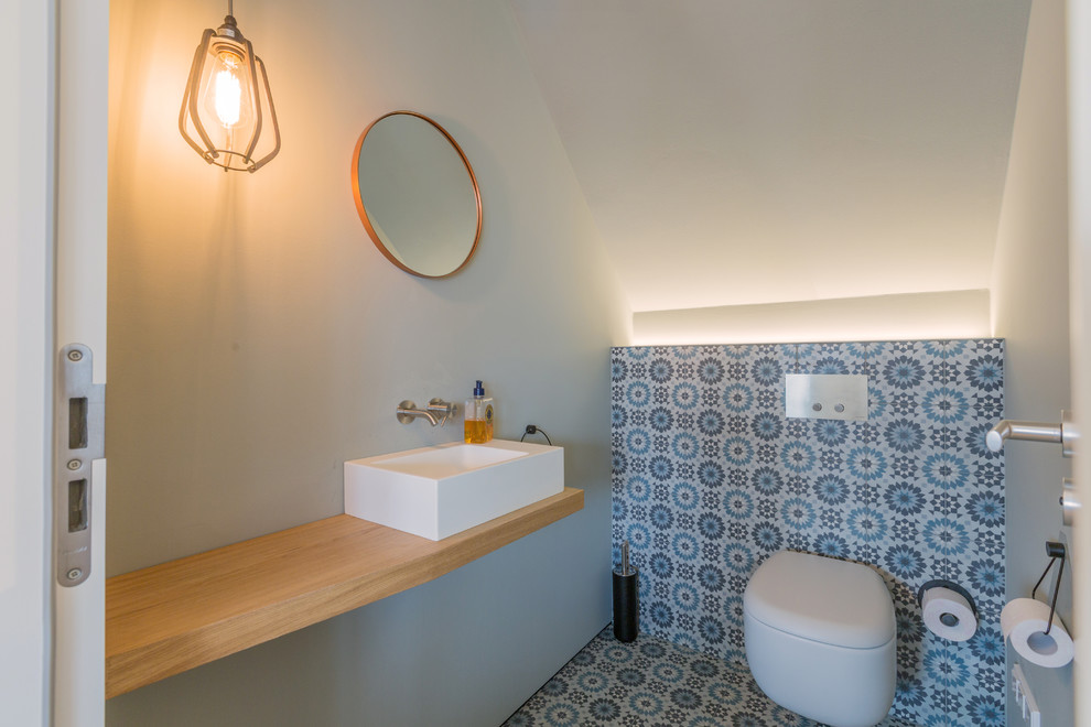 Idéer för att renovera ett litet 60 tals brun brunt toalett, med en vägghängd toalettstol, blå kakel, cementkakel, vita väggar, cementgolv, ett fristående handfat, träbänkskiva, flerfärgat golv och öppna hyllor