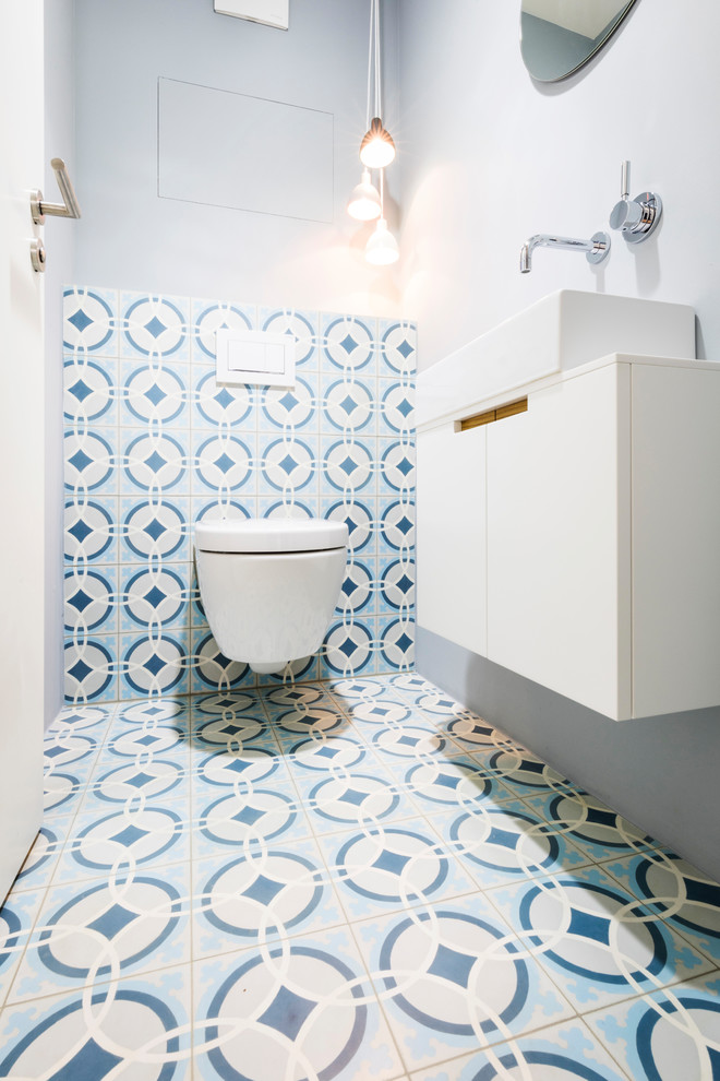 Example of a small trendy blue tile, white tile and cement tile cement tile floor and multicolored floor powder room design in Munich with flat-panel cabinets, white cabinets, a two-piece toilet, gray walls and a vessel sink