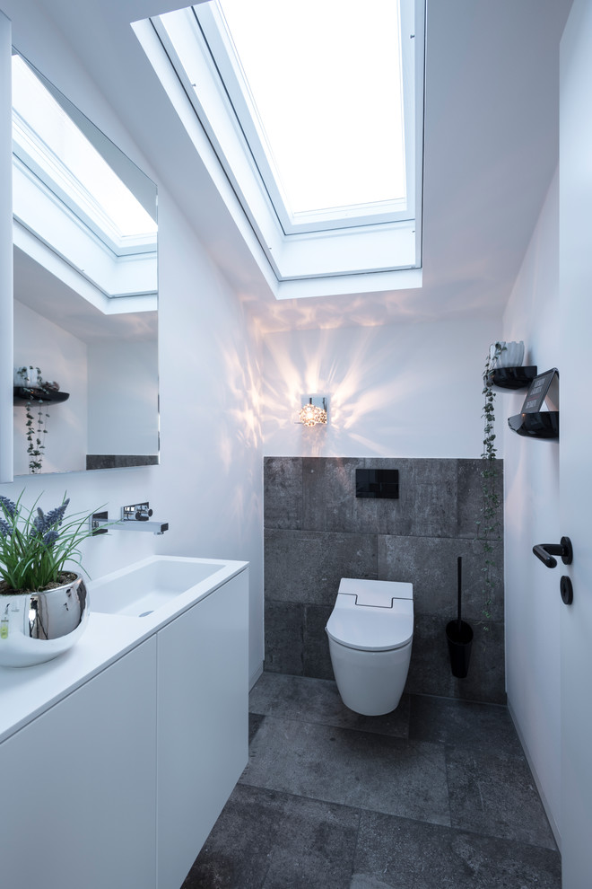 Ispirazione per un piccolo bagno di servizio design con ante lisce, ante bianche, WC a due pezzi, piastrelle nere, pareti bianche, lavabo integrato, pavimento nero e top bianco