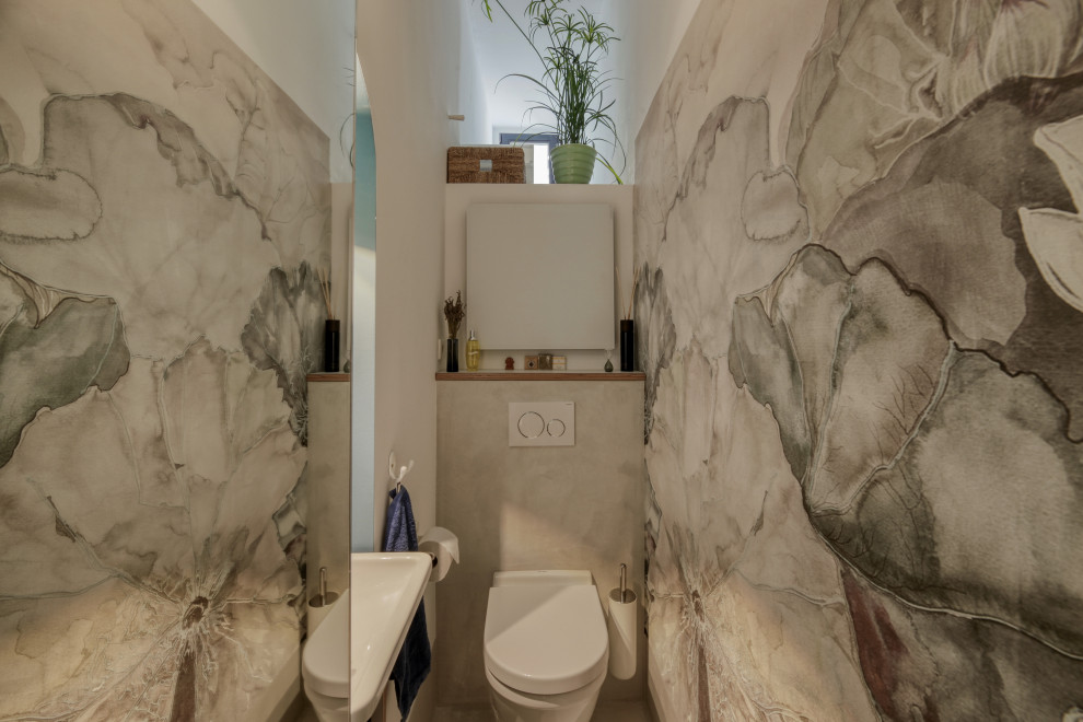 Inredning av ett modernt litet toalett, med en vägghängd toalettstol, grå kakel, vita väggar, ett väggmonterat handfat och grått golv