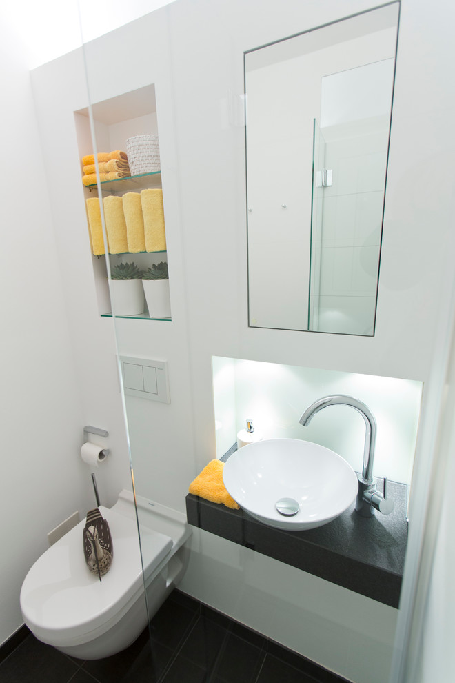 Ejemplo de aseo contemporáneo de tamaño medio con sanitario de pared, paredes blancas, lavabo sobreencimera, armarios abiertos y baldosas y/o azulejos negros