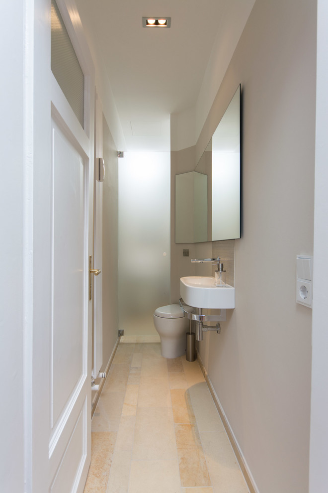 This is an example of a small contemporary cloakroom in Munich with flat-panel cabinets, white cabinets, a wall mounted toilet, beige tiles, limestone tiles, beige walls, limestone flooring, limestone worktops, beige floors and a wall-mounted sink.