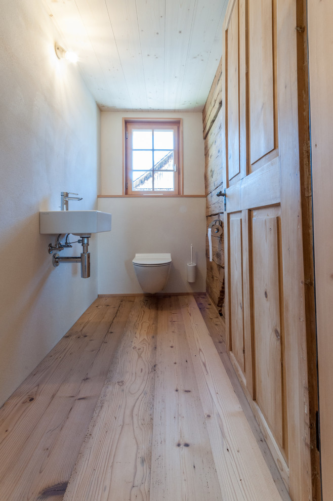 Example of a small cottage dark wood floor powder room design in Other with a wall-mount toilet, white walls, a wall-mount sink and solid surface countertops