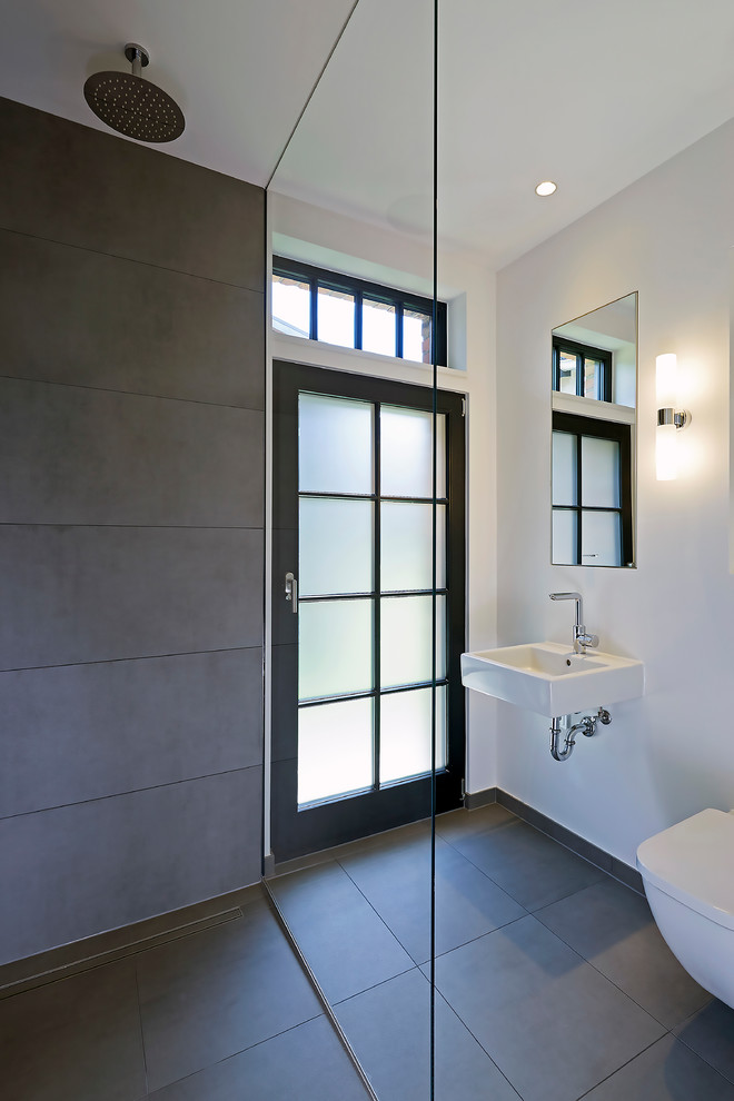 Exempel på ett litet modernt toalett, med en vägghängd toalettstol, grå kakel, cementkakel, vita väggar, cementgolv, ett väggmonterat handfat och grått golv