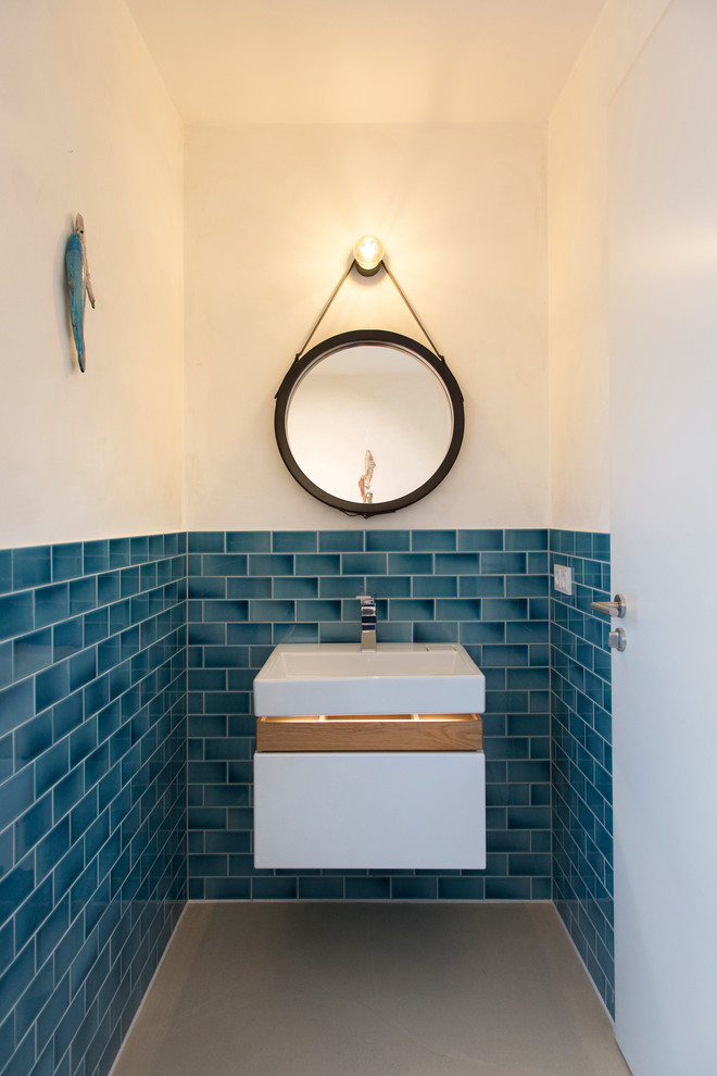 Cette image montre un petit WC et toilettes nordique avec un placard à porte plane, des portes de placard blanches, un carrelage bleu, un carrelage métro, un mur blanc, une vasque, un plan de toilette en bois et un plan de toilette marron.