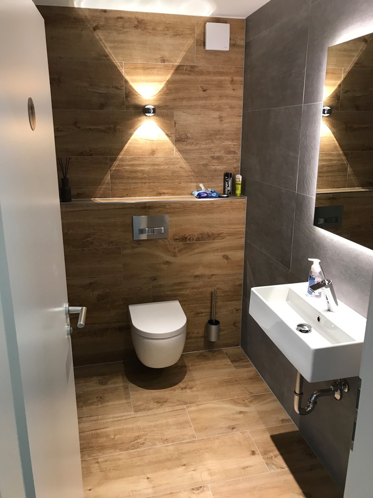 Kleine Urige Gästetoilette mit Wandtoilette mit Spülkasten, braunen Fliesen, schwarzen Fliesen, Wandwaschbecken und braunem Boden in Hannover