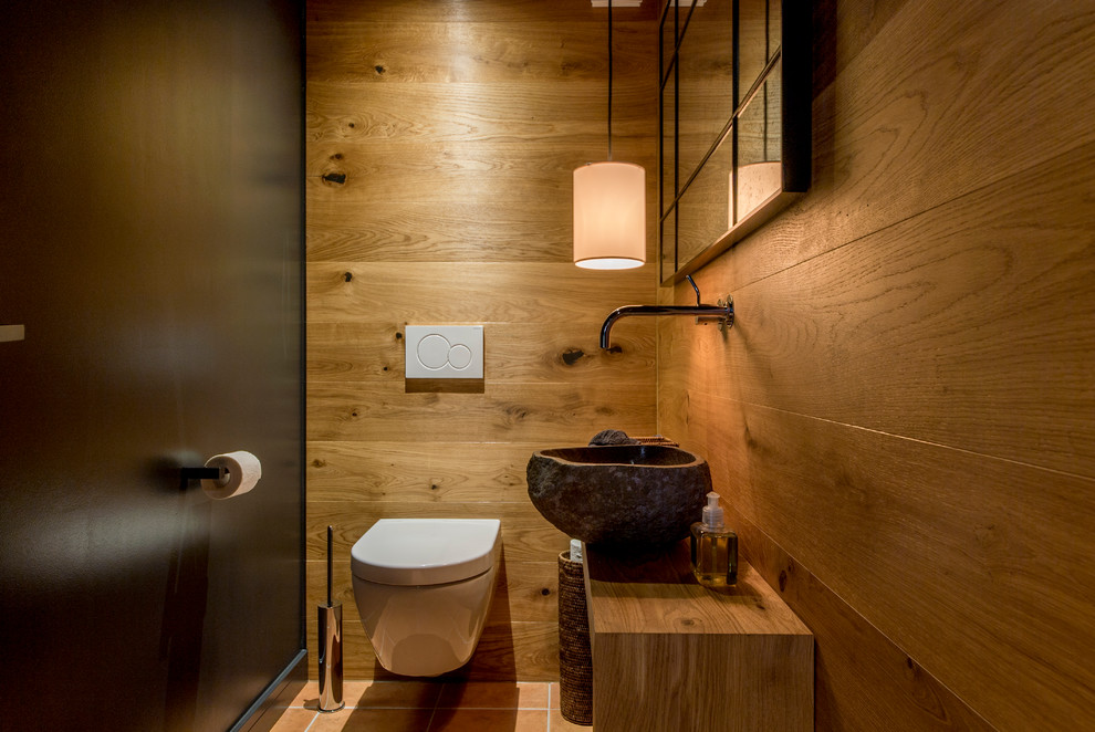 Cette photo montre un petit WC suspendu montagne en bois brun avec un mur noir, tomettes au sol, une vasque, un plan de toilette en bois, un sol rouge et un plan de toilette marron.