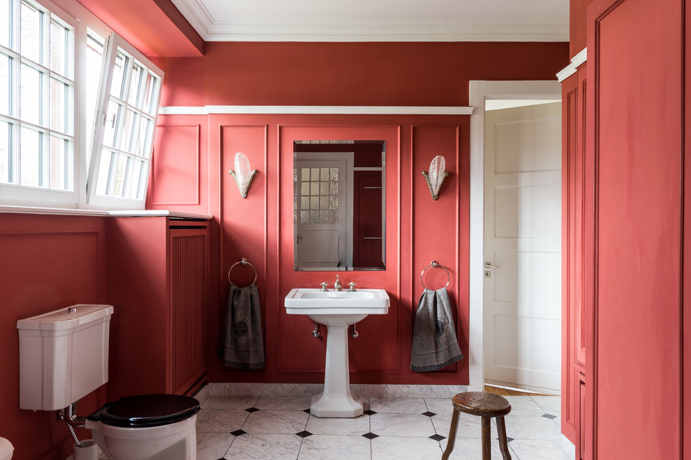 This is an example of a medium sized traditional cloakroom in Hamburg with a two-piece toilet, red walls, a pedestal sink, ceramic flooring and white floors.