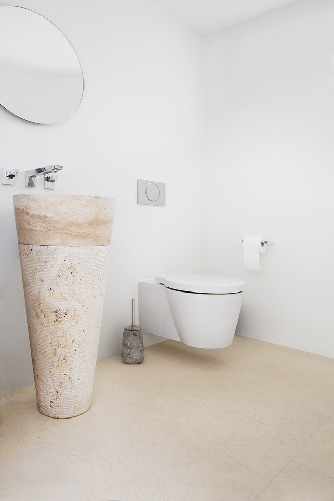 Idee per un piccolo bagno di servizio moderno con WC sospeso, pareti bianche, pavimento in pietra calcarea e lavabo a colonna