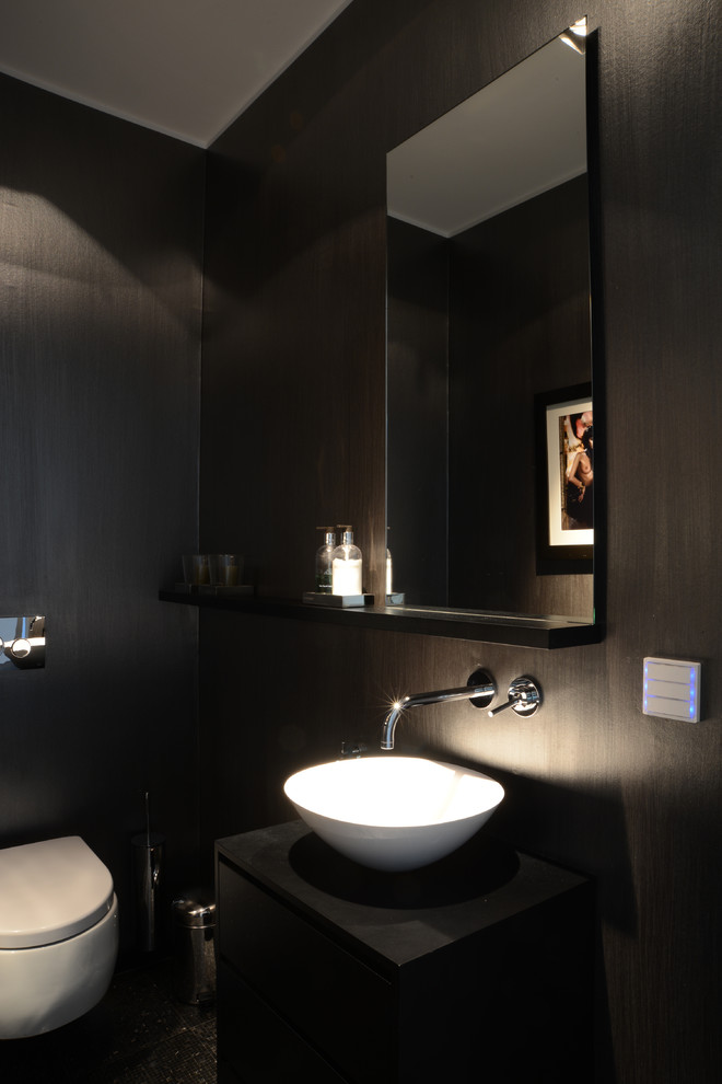 Cette photo montre un petit WC suspendu tendance avec un placard à porte plane, des portes de placard noires, un mur noir et une vasque.