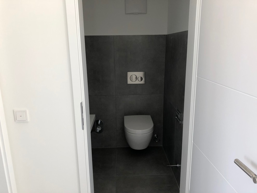 Ispirazione per un bagno di servizio design di medie dimensioni con WC a due pezzi, piastrelle grigie, piastrelle in pietra, pareti bianche, lavabo a bacinella, pavimento grigio e top bianco