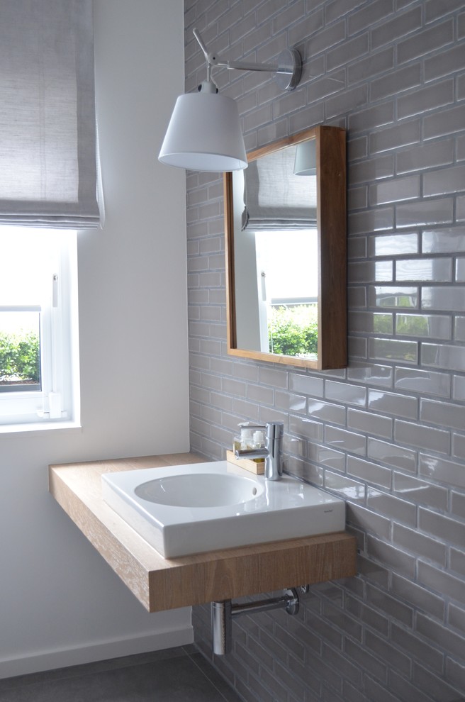 Пример оригинального дизайна: туалет в современном стиле с серой плиткой, настольной раковиной, столешницей из дерева, плиткой кабанчик, серыми стенами и бежевой столешницей