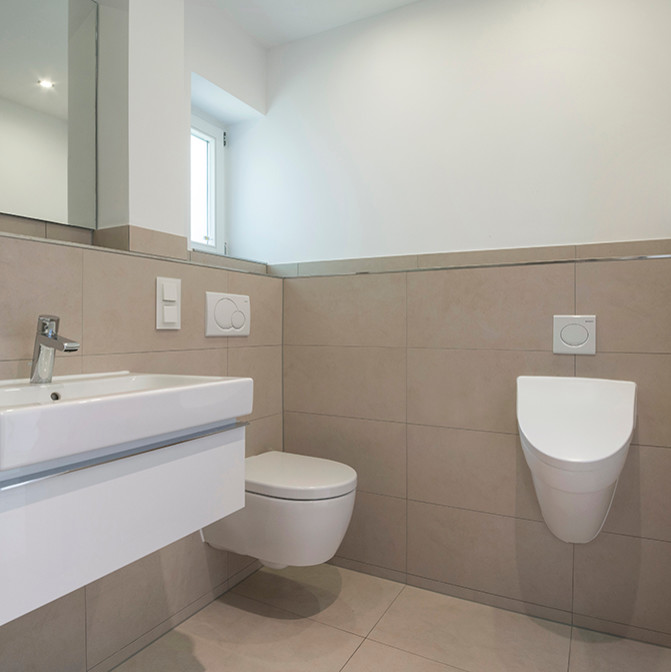 Modern inredning av ett mellanstort toalett, med släta luckor, vita skåp, en vägghängd toalettstol, beige kakel, beige väggar och ett väggmonterat handfat