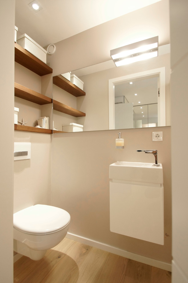 Bild på ett mellanstort funkis toalett, med en vägghängd toalettstol, beige väggar, ljust trägolv, ett väggmonterat handfat och öppna hyllor