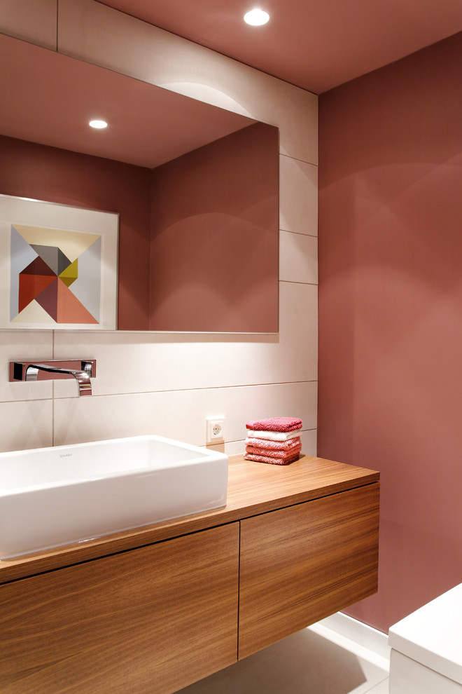 Inredning av ett modernt mellanstort brun brunt toalett, med ett fristående handfat, släta luckor, skåp i mellenmörkt trä, rosa väggar, vit kakel och träbänkskiva