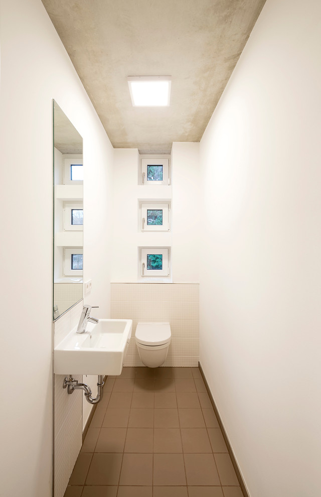 Exempel på ett litet modernt toalett, med en vägghängd toalettstol, brun kakel, vita väggar och ett väggmonterat handfat