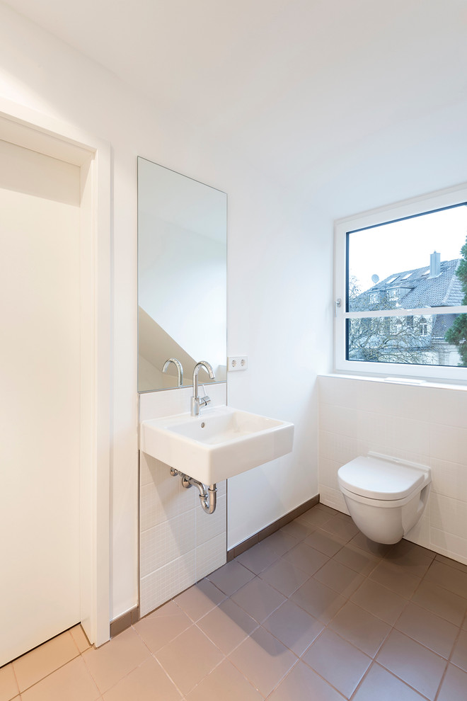 Réalisation d'un WC suspendu design de taille moyenne avec un mur blanc, un lavabo suspendu et un carrelage beige.
