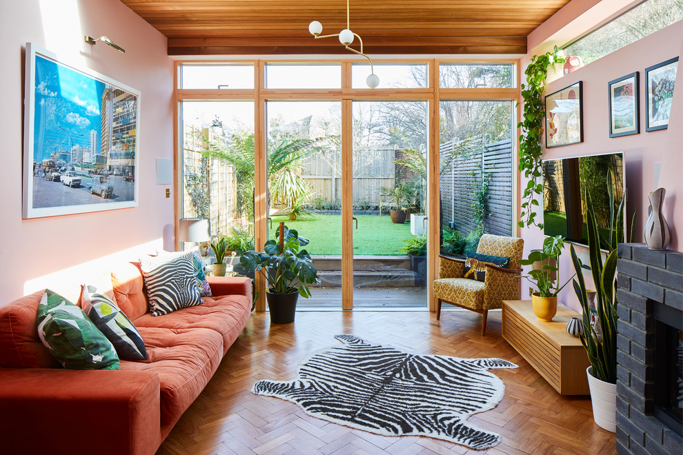 Retro Wohnzimmer mit rosa Wandfarbe, braunem Holzboden, Kaminumrandung aus Backstein und TV-Wand in London