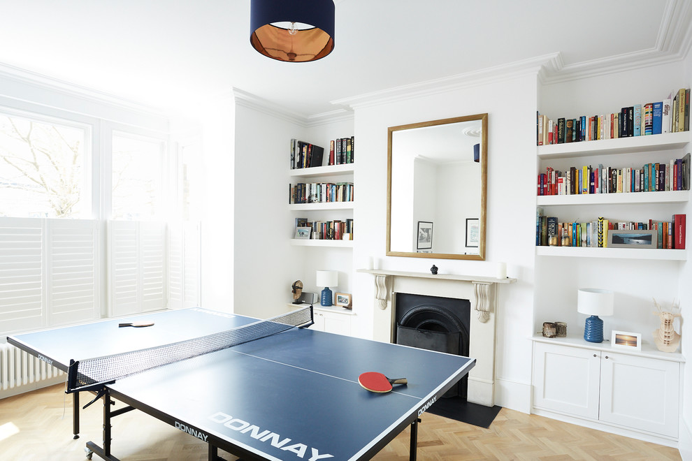 This is an example of a contemporary games room in London with a game room, white walls, light hardwood flooring, a standard fireplace and beige floors.