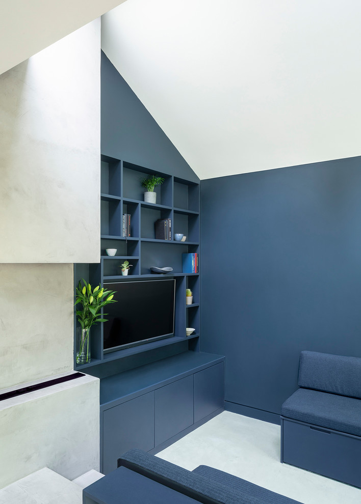 Modern inredning av ett mellanstort allrum med öppen planlösning, med ett bibliotek, blå väggar, betonggolv, en väggmonterad TV och grått golv