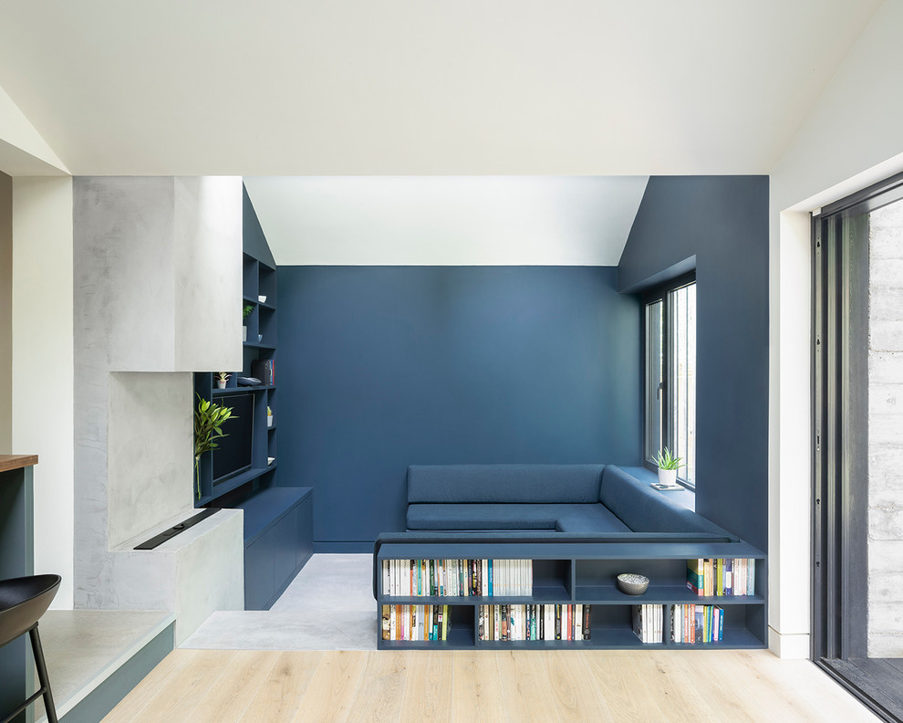Aménagement d'une salle de séjour moderne de taille moyenne et ouverte avec une bibliothèque ou un coin lecture, un mur bleu, sol en béton ciré, un téléviseur fixé au mur et un sol gris.