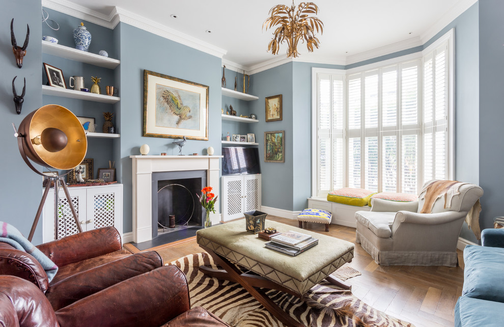 Example of a mid-sized eclectic medium tone wood floor and brown floor family room design in London with blue walls, a standard fireplace and a metal fireplace