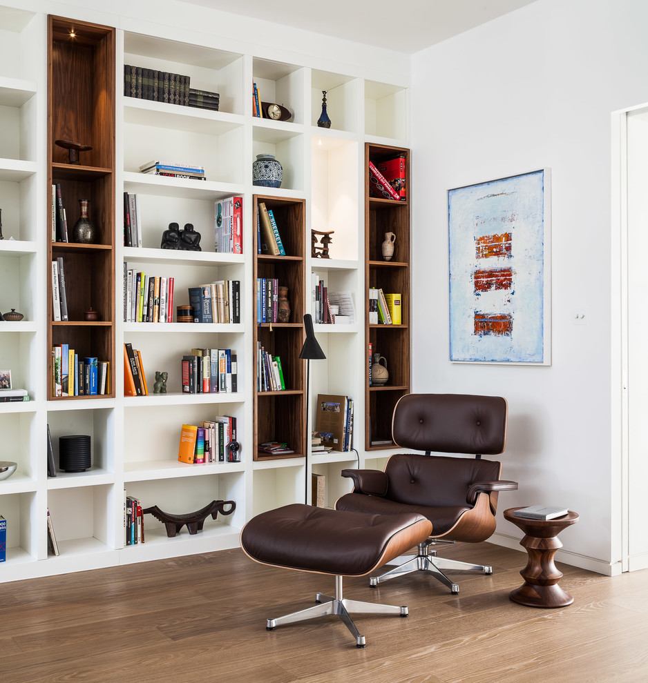 Diseño de sala de estar con biblioteca actual con paredes blancas y suelo de madera en tonos medios